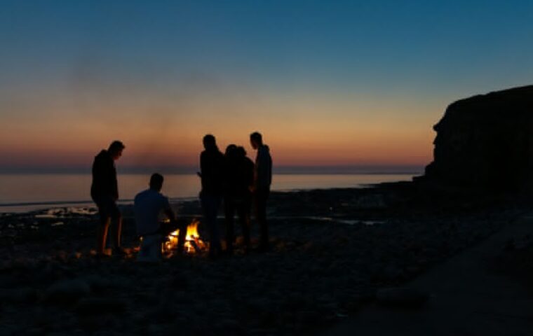 קבוצת אנשים מתכנסת סביב מדורה על חוף ים - אילוסטרציה למועצת שבט בהישרדות